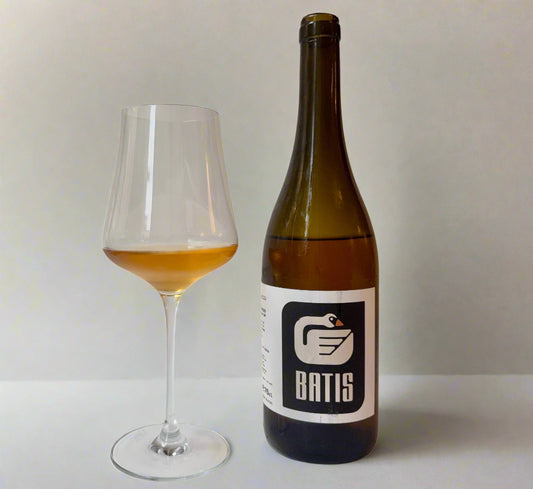 Wine bottle and glass with orange wine in it, with 'Batis' label on a plain background